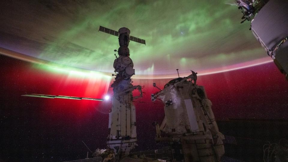 Eine Aurora auf der Erde, gesehen von der Raumstation. davor stehen verschiedene Raummodule