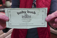 Bridgit Smith, executive director of the Insight Women's Center, holds a "Baby Buck," which its clients can earn for participating in classes and then use to get things such as car seats and cribs, Tuesday, Jan. 31, 2023, in Lawrence, Kan. The center provides both free prenatal and post-birth services to parents, and the Kansas Legislature is considering supporting such centers with both a tax credit for their donors and direct funding. (AP Photo/John Hanna)