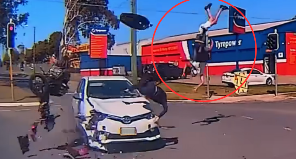 Image of the crash taking place, with three people flying through the air over a white Toyota Corolla.
