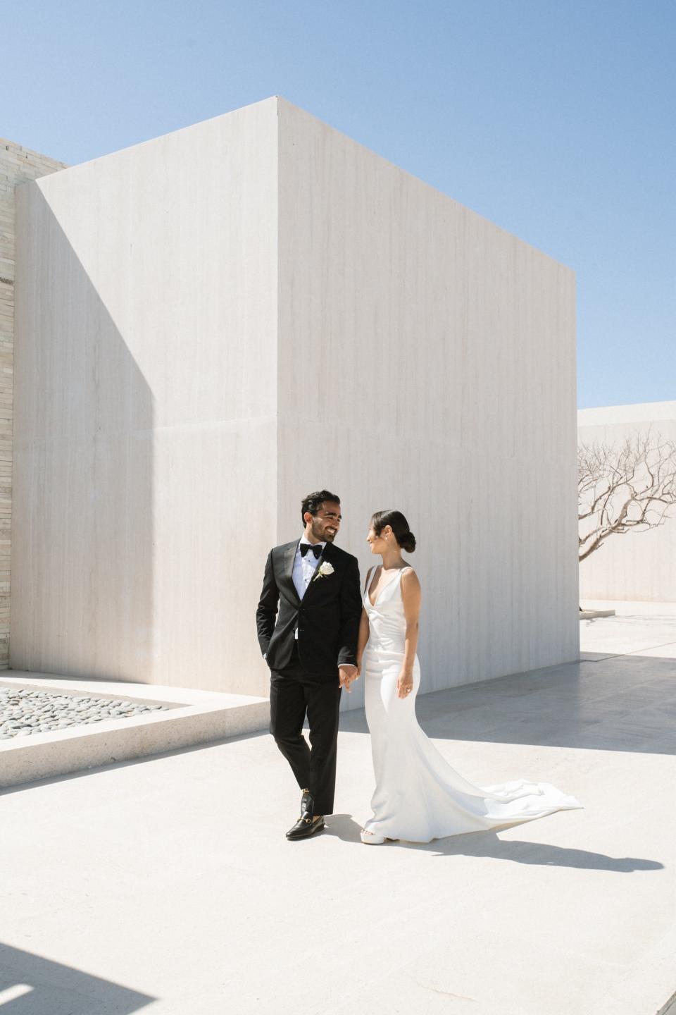 A bride and groom look at each other in their wedding attire and walk down a stone path.