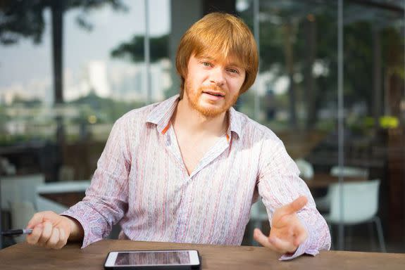 Portrait of grinning young man sitting at table and talking to business partner. Freelancer meeting with client at cafe and discussing project . Business and communication concept