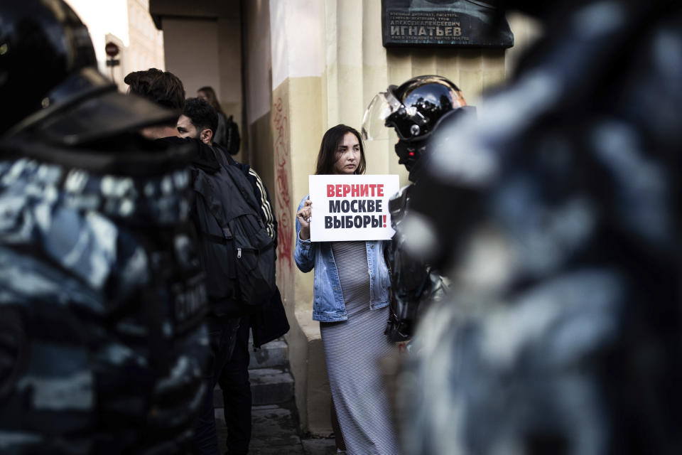 FILE - In this file photo taken on Saturday, Aug. 10, 2019, A woman holds a poster reading "Give us back our elections in Moscow!" in front of police during a protest in Moscow, Russia. Ella Pamfilova, head of Russian Central Election Commission, has defended the commission's decision to bar nearly two dozen candidates from running in a local Moscow election, which sparked a full-blown political crisis, but conceded that current election legislation is outdated and needs to be amended. (Evgeny Feldman, Meduza via AP, File)