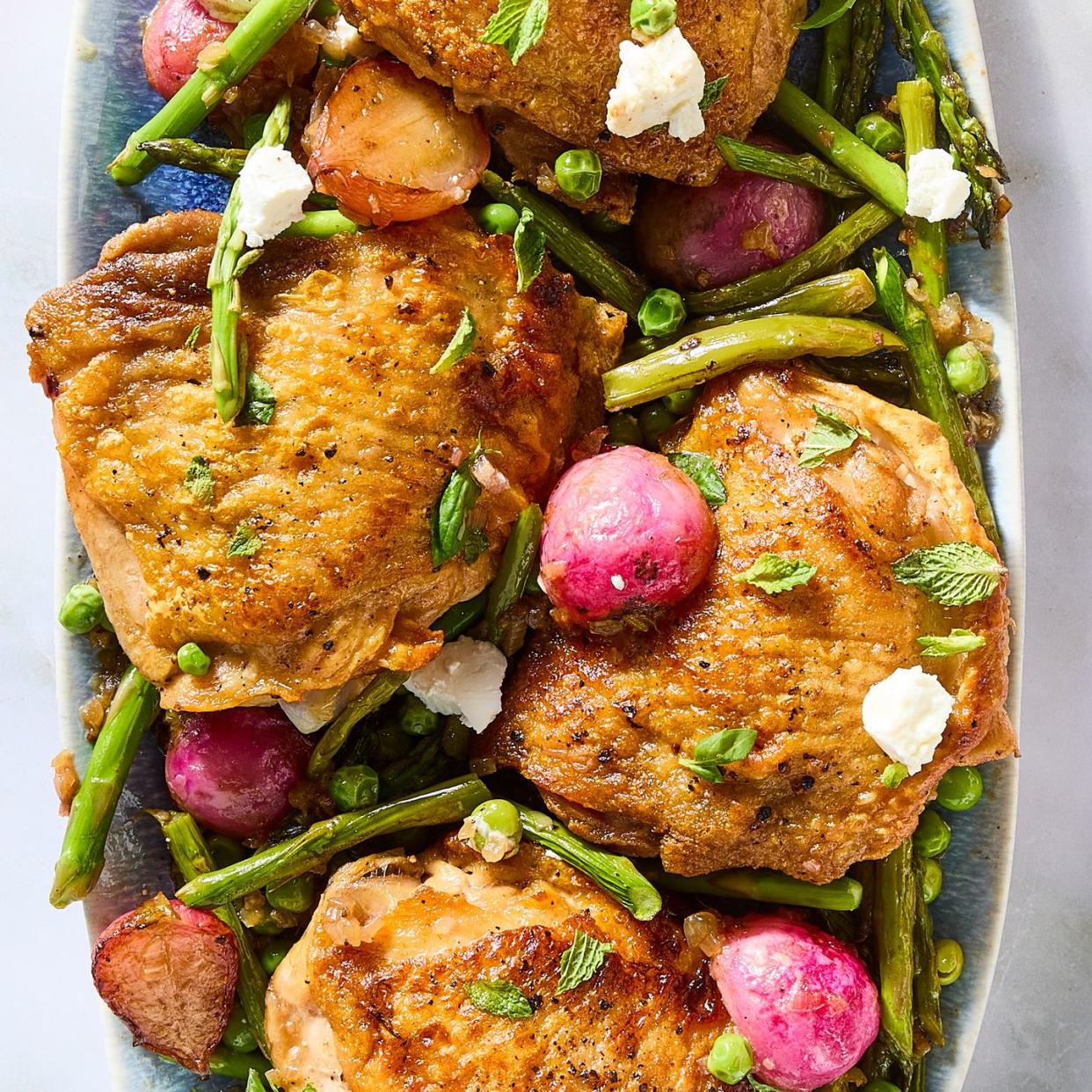 crispy chicken thighs with roasted radishes, asparagus, and peas on a platter