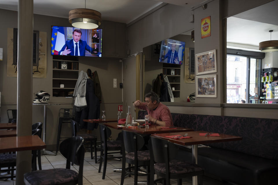 A man eats his lunch at a bar while French President Emmanuel Macron speaks with journalists on television in Marseille, southern France, Wednesday, March 22, 2023. Macron said Wednesday that the pension bill that he pushed through without a vote in parliament needs to be implemented by the "end of the year."(AP Photo/Daniel Cole)