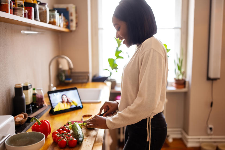 Woman video calling friend while cooking at home (Luis Alvarez / Getty Images)