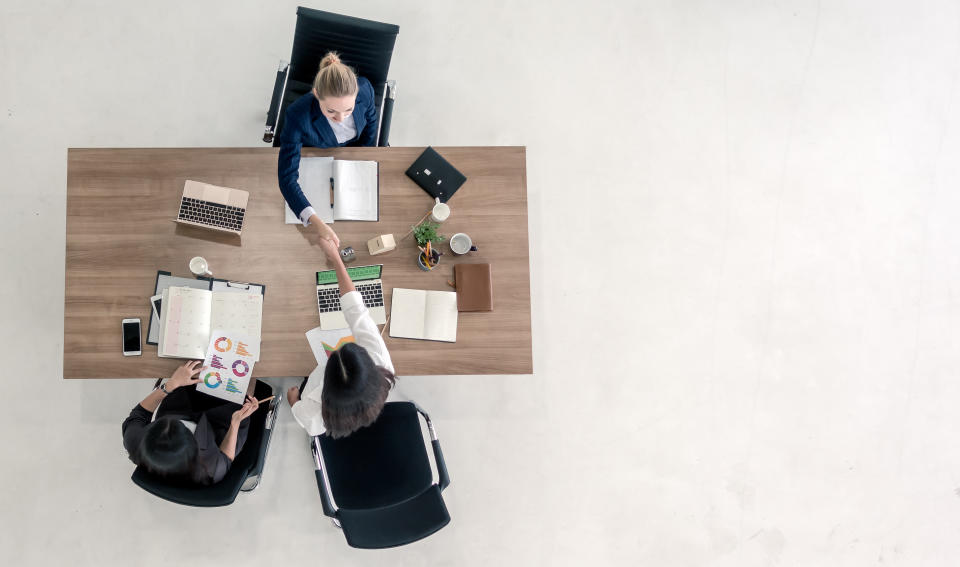 Top view of business people shaking hands after sealing a deal. High angle view of casual businesswomen handshake after concluding business agreement.