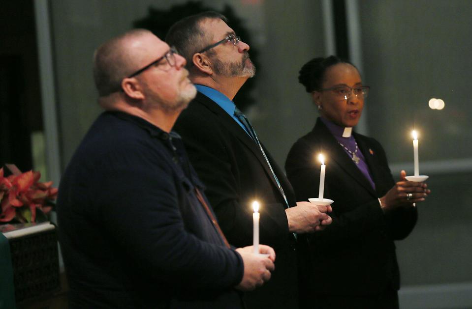 Jon Williams, pastor of First United Methodist Church of Perry, Ron Carlson and United Methodist Church Bishop Kennetha Bigham-Tsai pray during a candlelight vigil for the victims of the Perry High School shootings on Thursday.