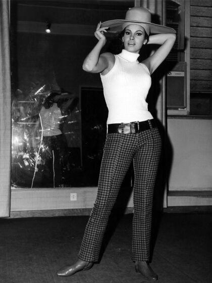 Woman, Raquel Welch wearing a wide brimmed hat and white tank top turtle neck, plaid pants and boots in black and white photo