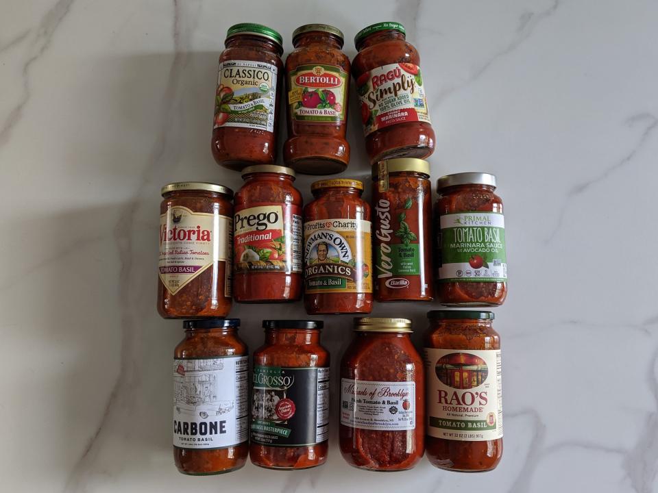 12 different jars of red pasta sauce laid out in three rows on a white kitchen counter