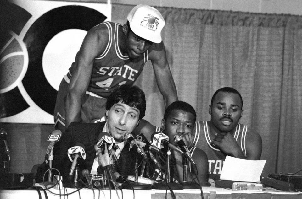 NC State coach Jim Valvano speaks to reporters at a press conference following the Wolfpack’s 1983 ACC Tournament championship game win. Behind Valvano is Thurl Bailey. At right are guards Dereck Wittenburg and Sidney Lowe.