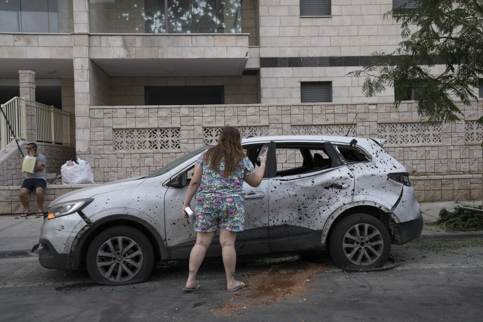 A woman takes a photo of a car that was hit by a rocket fired from the Gaza Strip, in the southern Israeli city of Ashkelon, Israel, Saturday, Aug. 6, 2022. (AP Photo/Maya Alleruzzo)