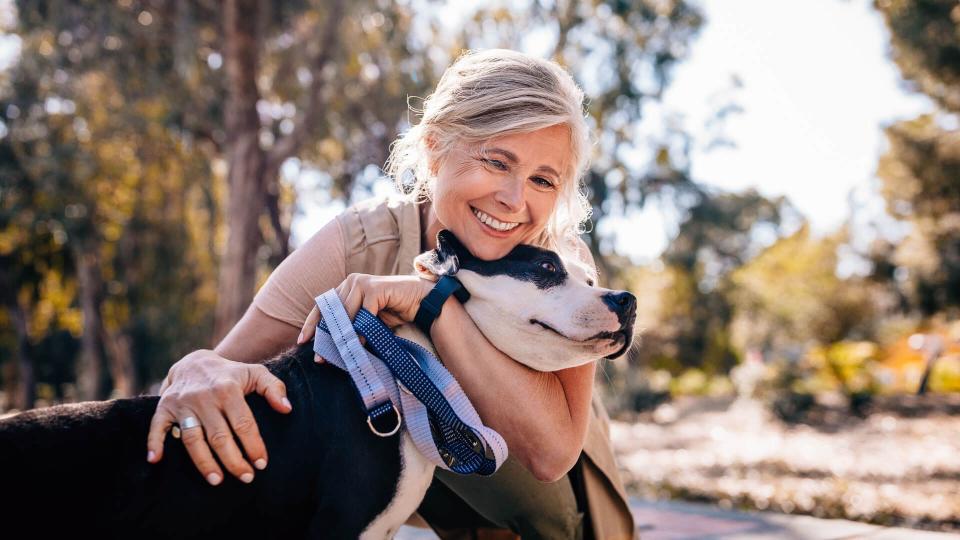 Happy senior woman enjoying walk in nature and embracing pet dog in forest park.