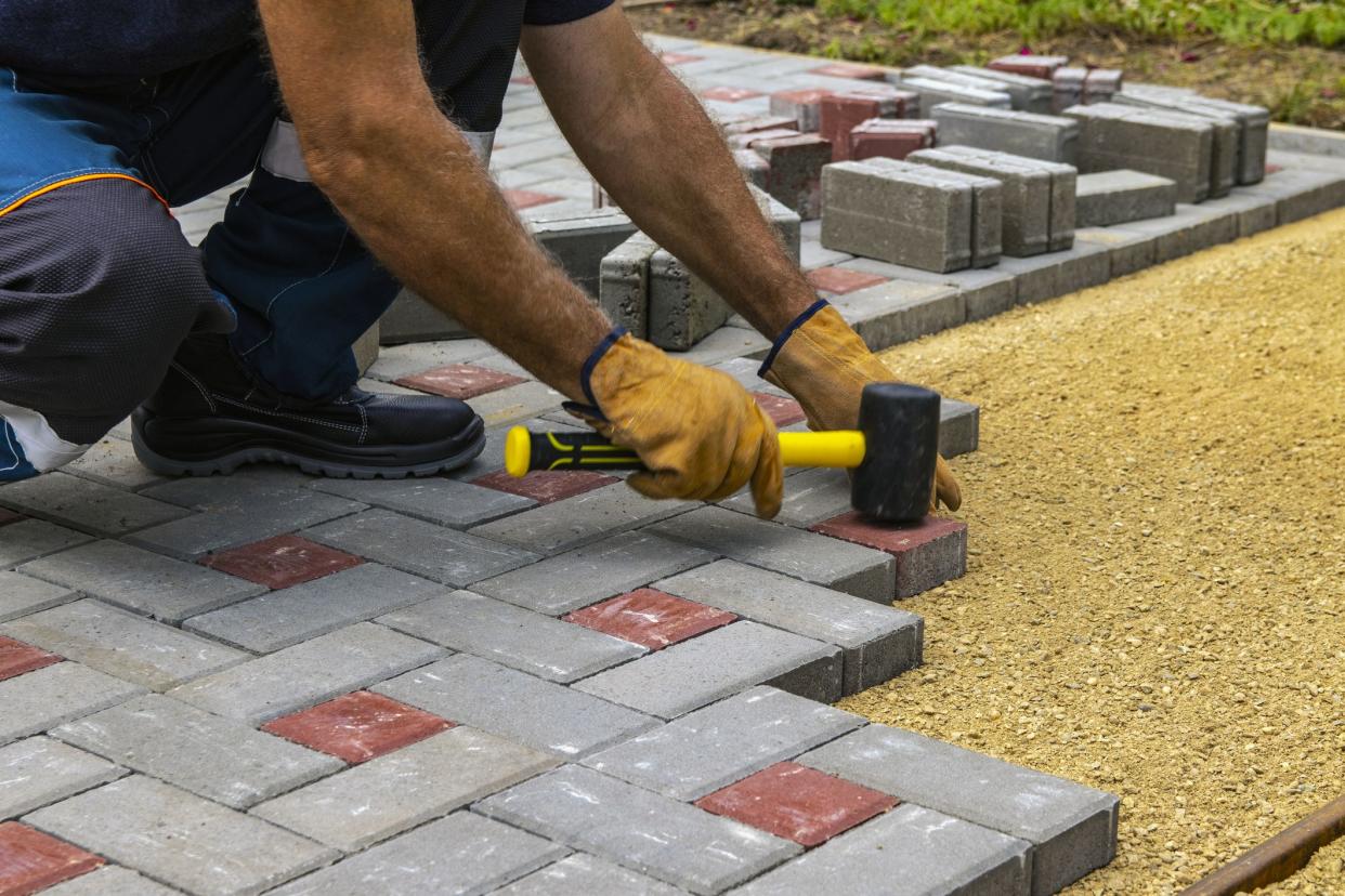 Professional bricklayers install new tiles or slabs for the roadway, sidewalks or patio on a foundation of lined sand. Laying gray concrete paving slabs in the courtyard of the house.