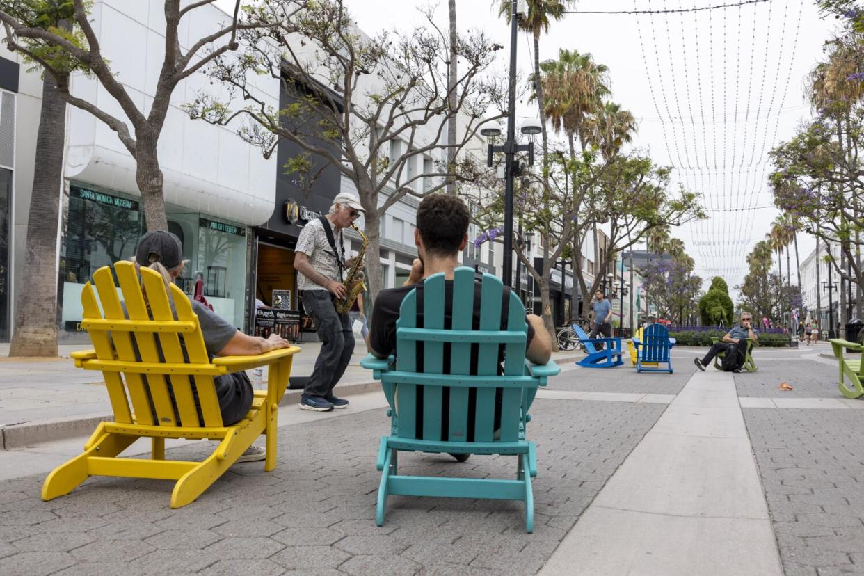 People in Adirondack chairs listen to a saxophone player.