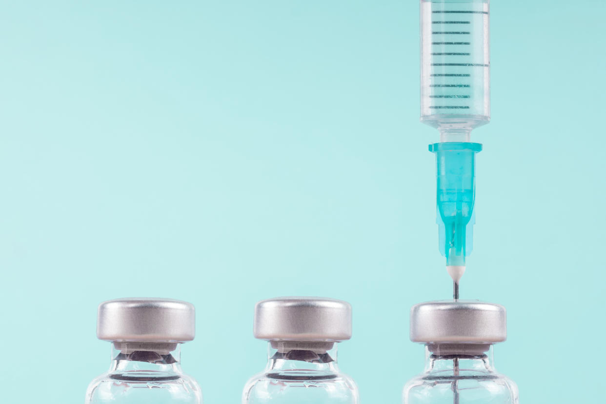 A needle withdraws vaccine from one of three vials.