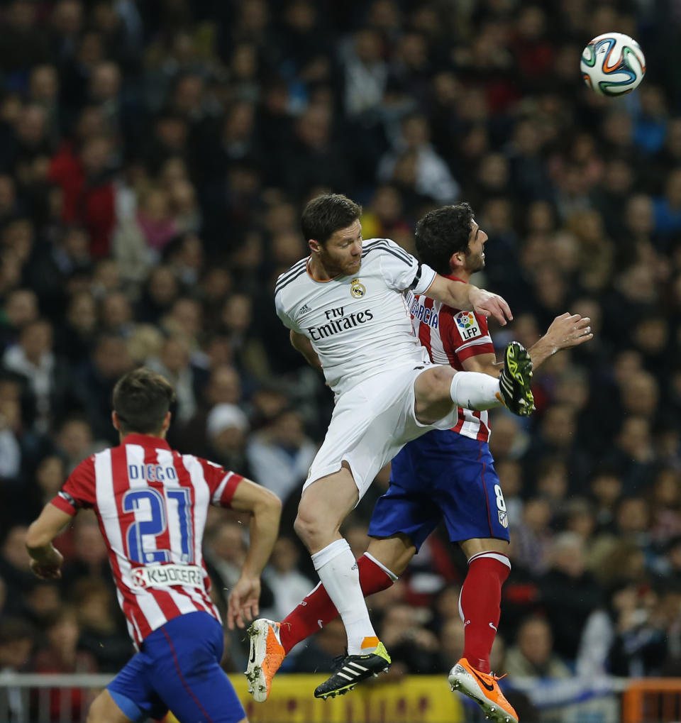 Real's Xabi Alonso, center, and Atletico's Raul Garca, right, jump for a high ball during a semifinal, 1st leg, Copa del Rey soccer derby match between Real Madrid and Atletico Madrid at the Santiago Bernabeu Stadium in Madrid, Wednesday Feb. 5, 2014. (AP Photo/Paul White)