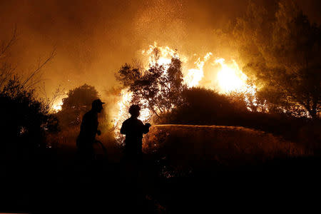 Firefighters are silhouetted as they try to extinguish a wildfire burning near the village of Kalamos, north of Athens, Greece, August 13, 2017. REUTERS/Costas Baltas