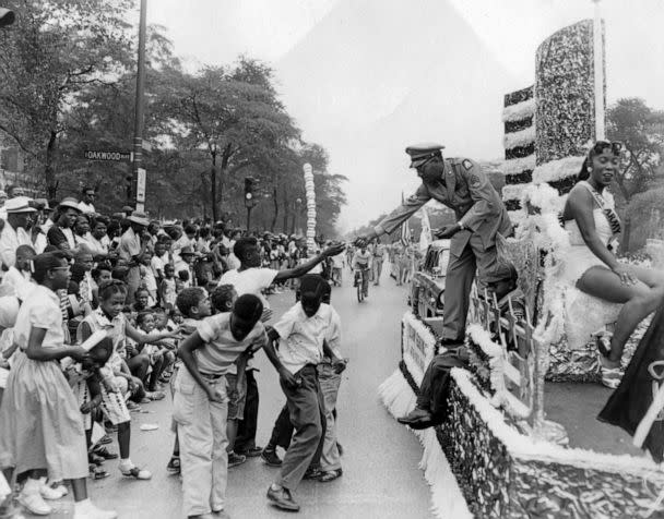 PHOTO: A uniformed officer hands treats and candies out to members of the crowd watching the annual Bud Billiken parade, sponsored by the Chicago Defender, in Chicago, in 1984.  (Robert Abbott Sengstacke/The Abbott Sengstacke Family Papers via Getty Images)