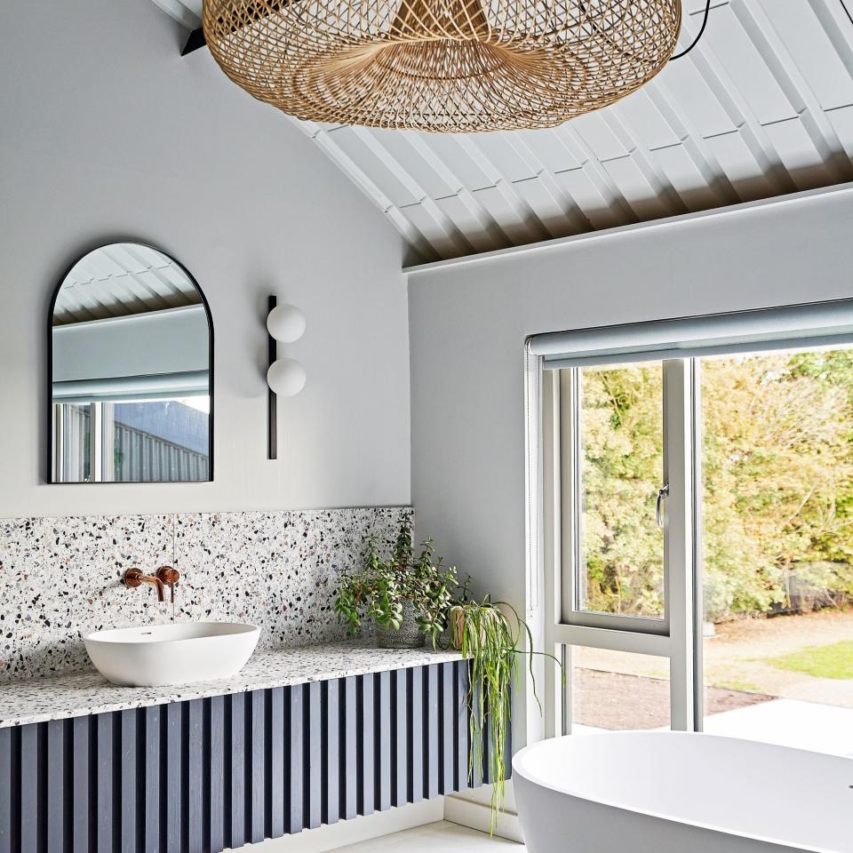 bathroom overlooking garden with freestanding bath, marble sink area and rattan light shade