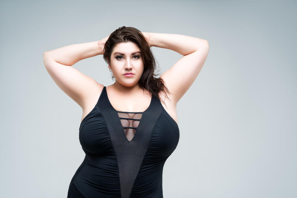 Sexy plus size fashion model in black one-piece swimsuit, woman in lingerie on gray background, body positive concept