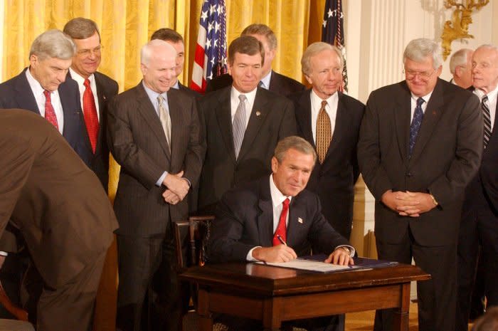 Surrounded by members of Congress, President George W. Bush signs the congressional resolution authorizing U.S. use of force against Iraq if needed, during a ceremony in the East Room of the White House on October 16, 2002. File Photo by Chris Corder/UPI