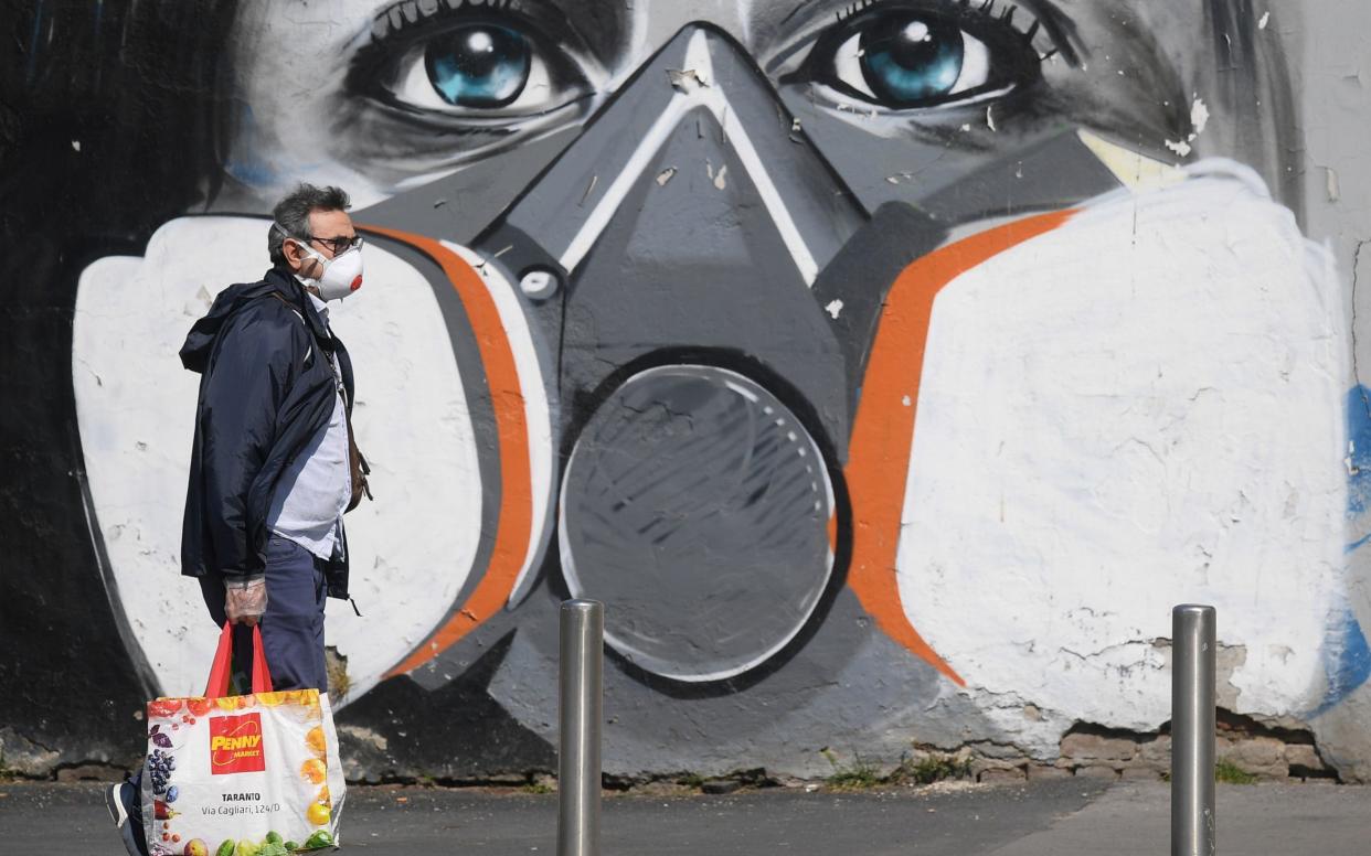A man walks past coronavirus artwork in Milan - Reuters