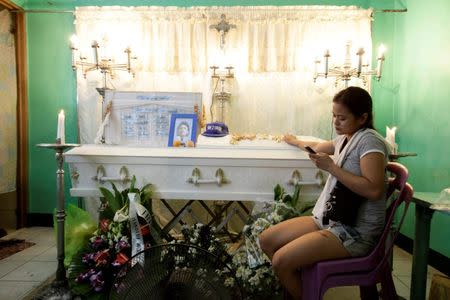 Jennelyn Olaires, 26, uses her mobile phone as she sits beside the coffin of her partner Michael Siaron in Pasay, Metro Manila, Philippines July 28, 2016. REUTERS/Czar Dancel