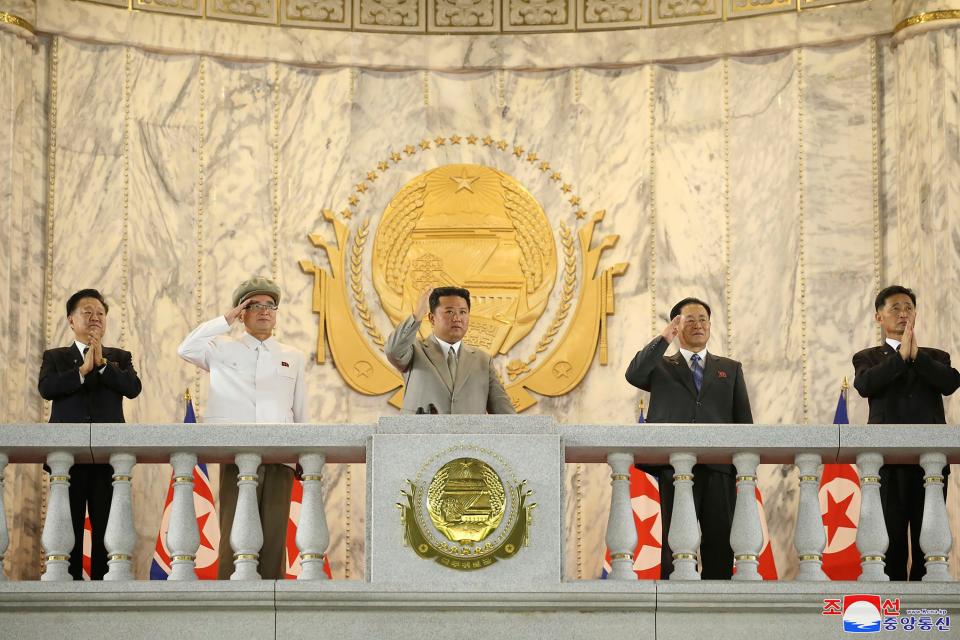 The North Korean leader Kim Jong Un, center, waves from a balcony toward the assembled troops and spectators.