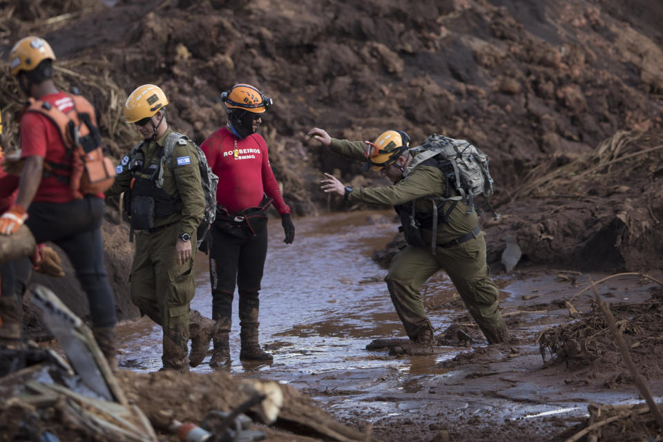 An Israeli rescue specialist, right, arrives at a site where a body was found inside a vehicle stuck in the mud, days after a dam collapse in Brumadinho, Brazil, Monday, Jan. 28, 2019. Firefighters on Monday carefully moved over treacherous mud, sometimes walking, sometimes crawling, in search of survivors or bodies four days after a dam collapse that buried mine buildings and surrounding neighborhoods with iron ore waste. (AP Photo/Leo Correa)