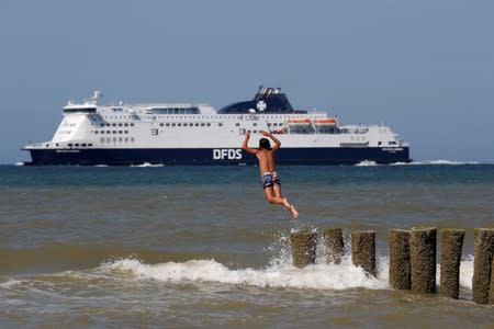 A boy jumps into the sea on a hot summer day as a ferry sails past the beach in Sangatte