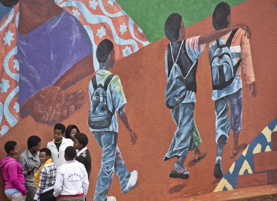 In this photo taken Monday, March 24, 2014, Rwandan students standing next to a mural talk amongst themselves after finishing an examination and waiting to eat lunch at the Agahozo-Shalom Youth Village near Rwamagana, in Rwanda. Most of the kids in a school set amid the lush green, rolling hills of eastern Rwanda don't identify themselves as Hutu or Tutsi. That's a positive sign for Rwanda, which is now observing the 20th anniversary of its genocide, a three-month killing spree that, according to the official Rwandan count, left more than 1 million people dead, most of them Tutsis killed by Hutus. The teenagers attending the Agahozo-Shalom Youth Village, a school with dorms that creates tight-knit student families, say the ethnic slaughter that their parents or grandparents were a part of either as victims or perpetrators won't be repeated. The school director echoes the sentiment. (AP Photo/Ben Curtis)