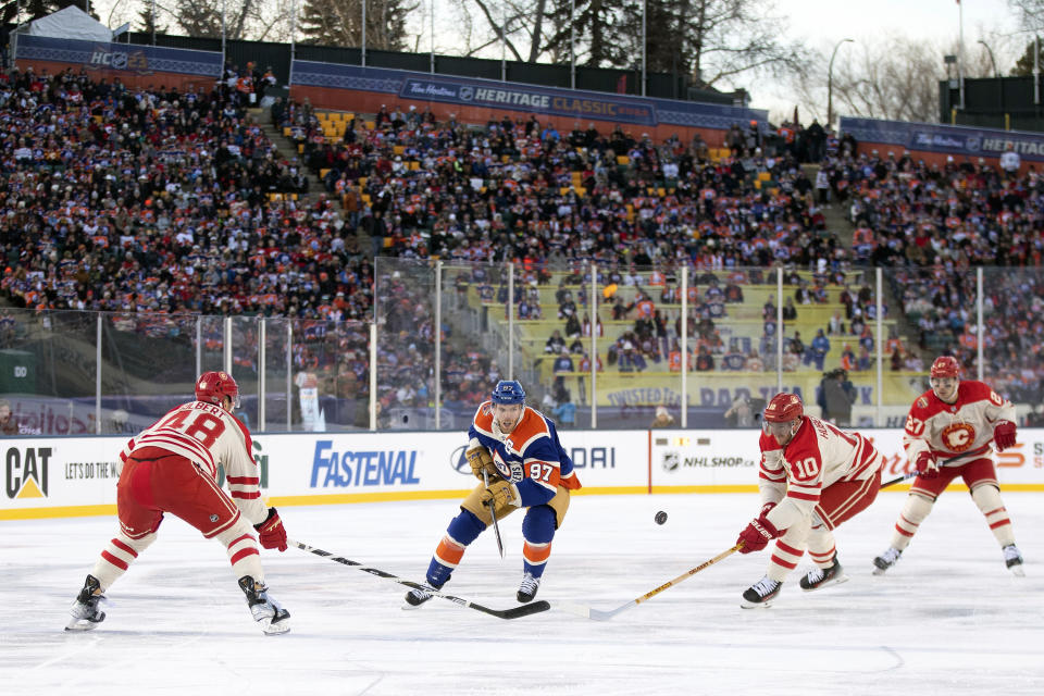 Calgary Flames' Dennis Gilbert (48), Jonathan Huberdeau (10) and Matthew Coronato (27) defend against Edmonton Oilers' Connor McDavid (97) during first-period NHL Heritage Classic outdoor hockey game action in Edmonton, Alberta, Sunday, Oct. 29, 2023. (Jason Franson/The Canadian Press via AP)