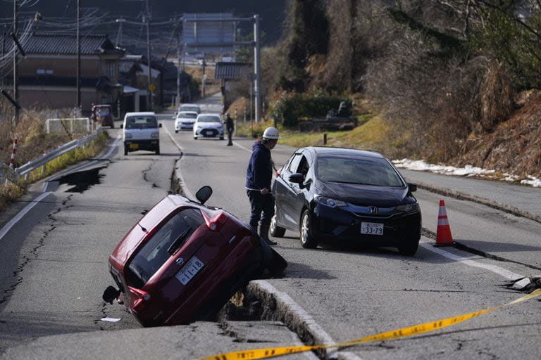 Un hombre dirige a un conductor que se desplaza por una calle dañada cerca de la ciudad de Anamizu en la península de Noto frente al Mar de Japón, al noroeste de Tokio, el martes 2 de enero de 2024, tras el mortal terremoto del lunes.