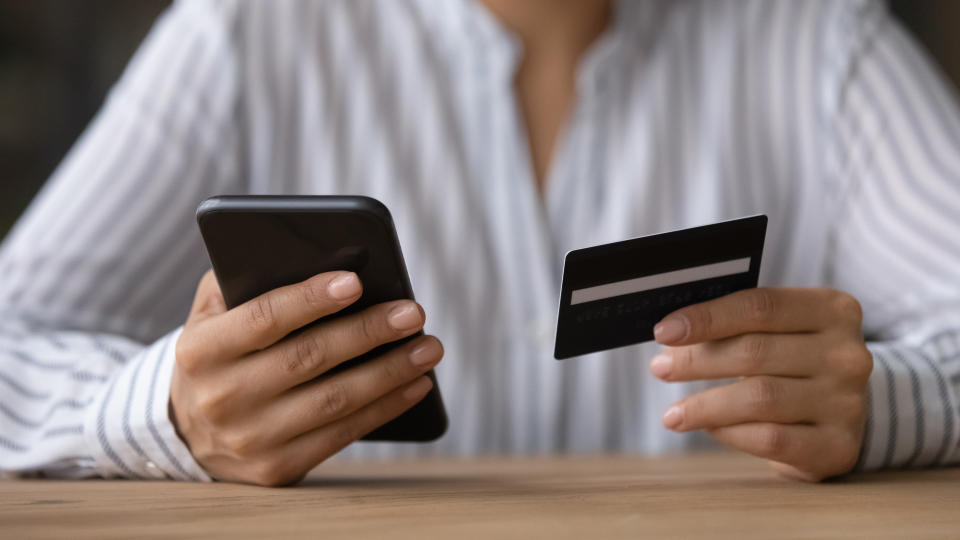 Close up woman paying online by credit card, using smartphone, sitting at wooden desk, young female holding phone, browsing banking service, checking balance, shopping, making internet payment