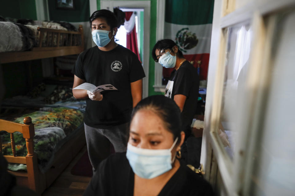 Family members wear personal protective equipment as the Rev. Fabian Arias performs an in-home service beside the remains of Raul Luis Lopez who died from COVID-19 the previous month, Saturday, May 9, 2020, in the Corona neighborhood of the Queens borough of New York. (AP Photo/John Minchillo)