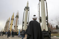 FILE - In this Feb. 3, 2019 file photo, an Iranian clergyman looks at domestically built surface to surface missiles displayed by the Revolutionary Guard in a military show marking the 40th anniversary of the Islamic Revolution, at Imam Khomeini Grand Mosque in Tehran, Iran. On Monday, April 8, 2019, the Trump administration designated Iran’s Revolutionary Guard a “foreign terrorist organization” in an unprecedented move against a national armed force. Iran’s Revolutionary Guard Corps went from being a domestic security force with origins in the 1979 Islamic Revolution to a transnational fighting force. (AP Photo/Vahid Salemi, File)