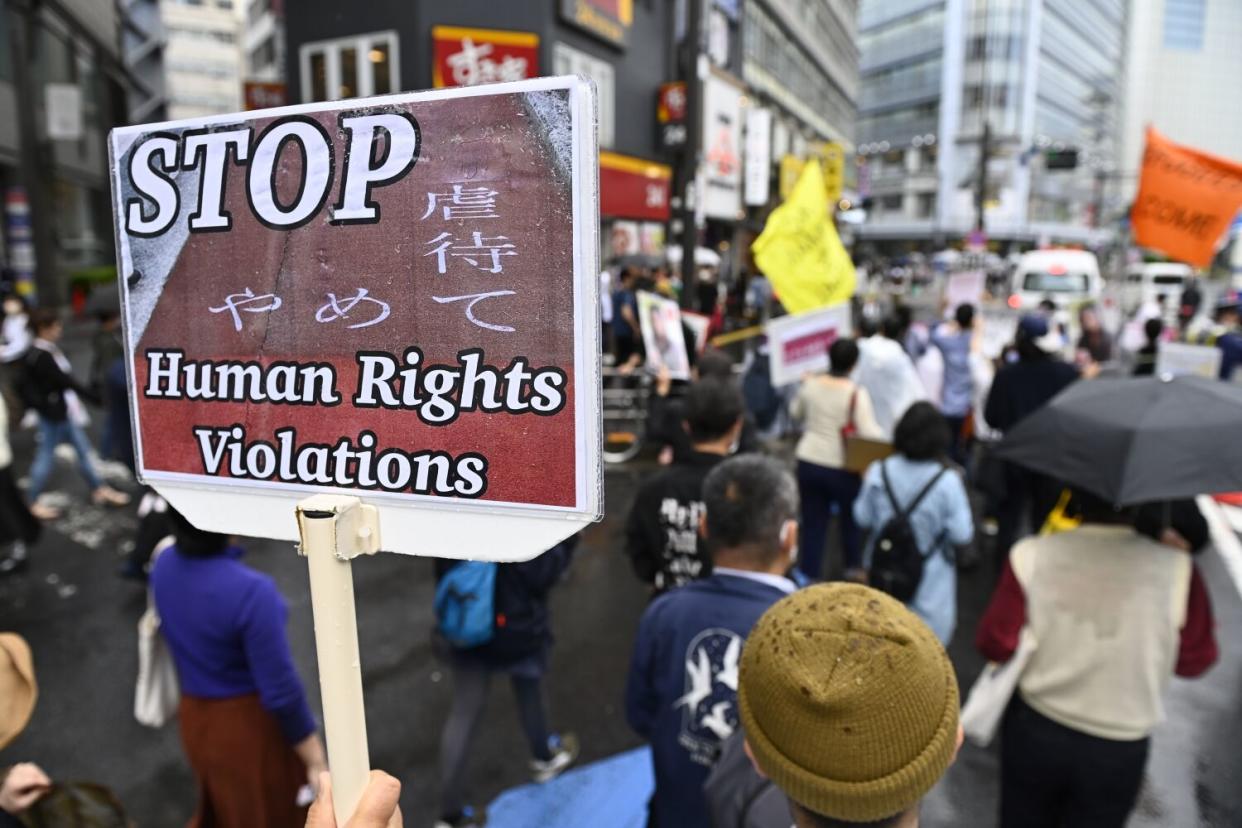 People protest in the street, one holding a sign reading, "Stop human rights violations."