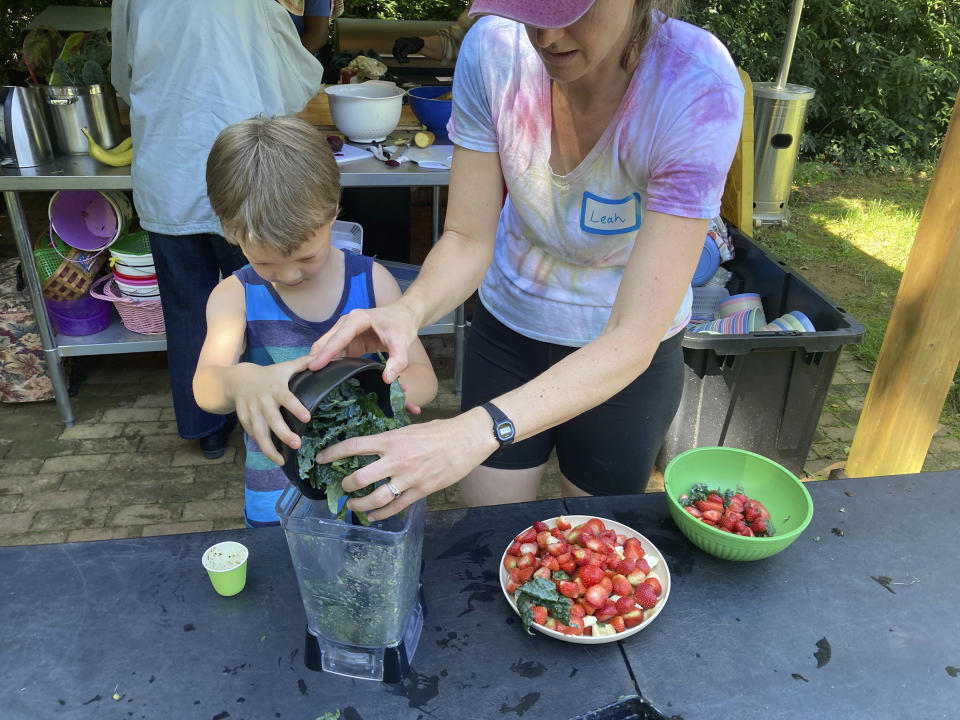 Grow It organizer Leah Reichardt-Osterkatz, right, helps children make smoothies from strawberries they picked, plus kale grown on the farm, at Spring Forest in Hillsborough, N.C., on Wednesday, May 29, 2024. (Yonat Shimron/Religion News Service via AP)