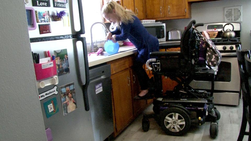 Kelly Boyd raises her the seat of her wheelchair to wash dishes in her Hamilton Township home Wednesday, November 1, 2023. She spoke about the delays that the disability community faces when their wheelchair needs repairs.