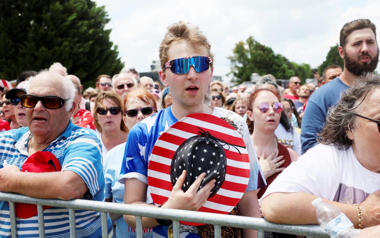 Trump supporters clasp their MAGA hats as they wait for former president to appear at a rally