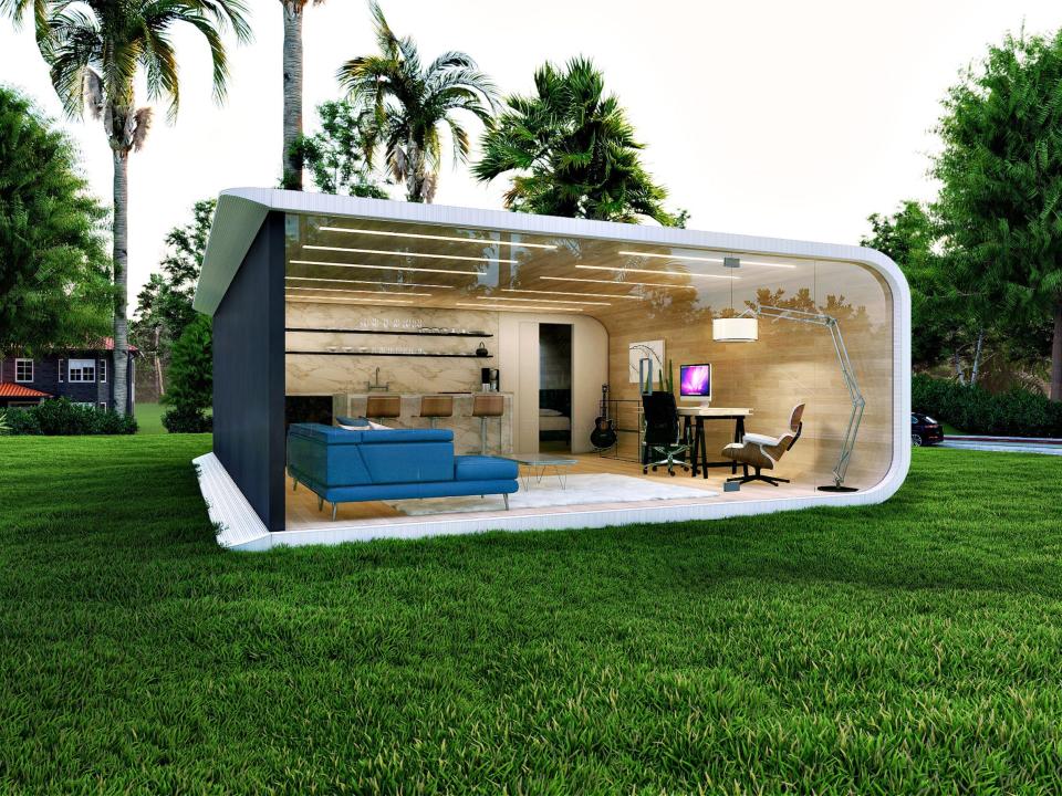The ADU in a backyard on a patch of grass. There's furniture inside d inside.