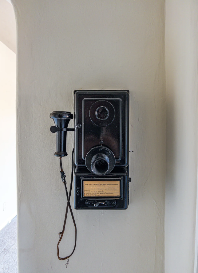 Vintage wall telephone with rotary dial, handset and a small board with instructions. No people can be seen in the picture.