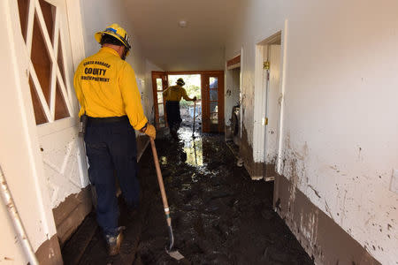 Santa Barbara County Firefighters Rick Pinal and Vince Agapito climb through a home destroyed by mudflow and debris in Montecito, California, U.S,. January 13, 2018. Mike Eliason/Santa Barbara County Fire/Handout via REUTERS