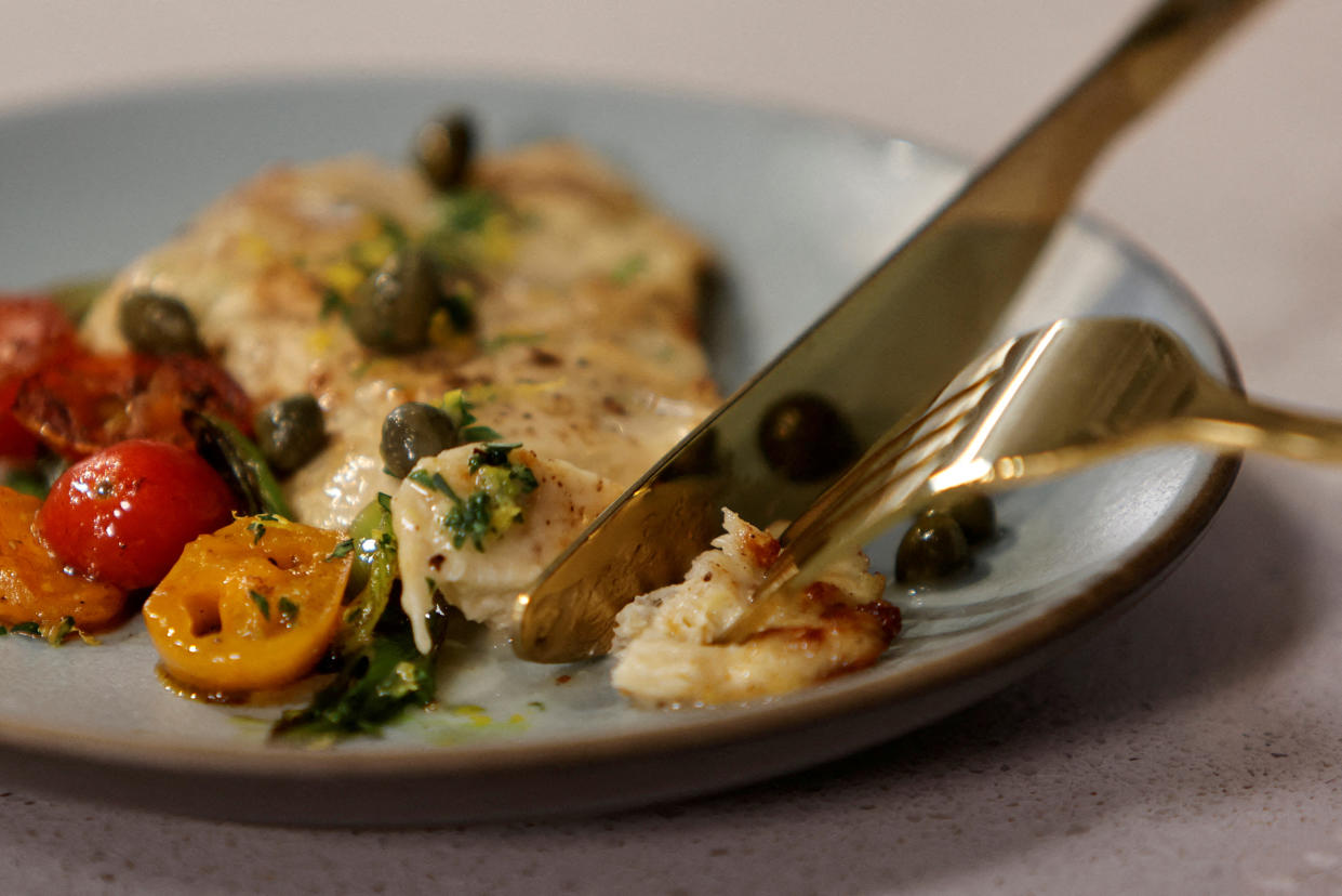 A diner cuts off a piece of an unctuous looking piece of pan-fried cultivated chicken breast with cherry tomatoes and herbs.