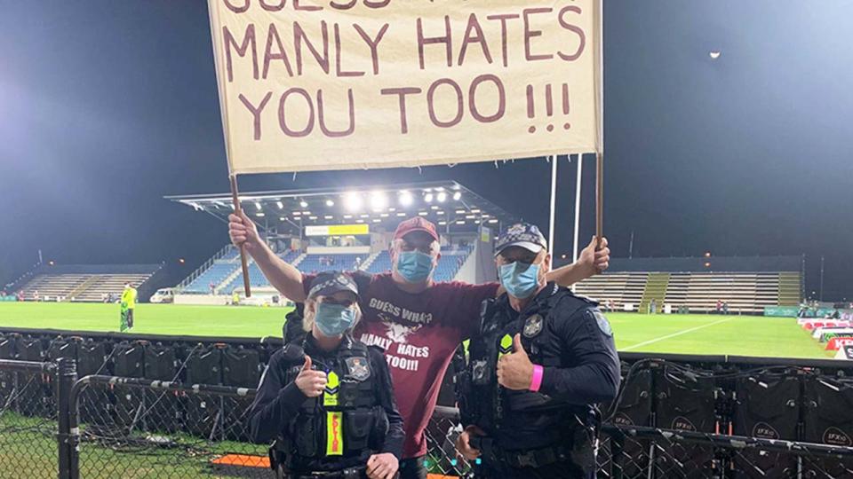 Manly fan Stephen Lucas poses with two police officers, while holding his sign.