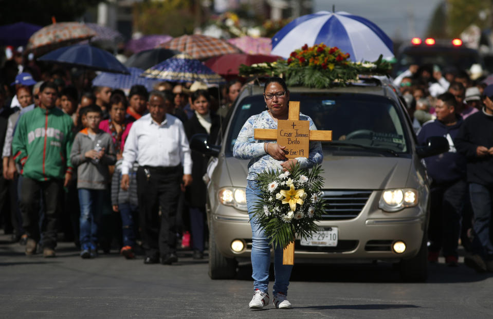 A woman carries a cross with the name Cesar Jimenez Brito during his funeral procession after he died when a gas pipeline exploded in the village of Tlahuelilpan, Mexico, Sunday Jan. 20, 2019. A massive fireball that engulfed locals scooping up fuel spilling from a pipeline ruptured by thieves in central Mexico killed dozens of people and badly burned dozens more on Jan. 18. (AP Photo/Claudio Cruz)