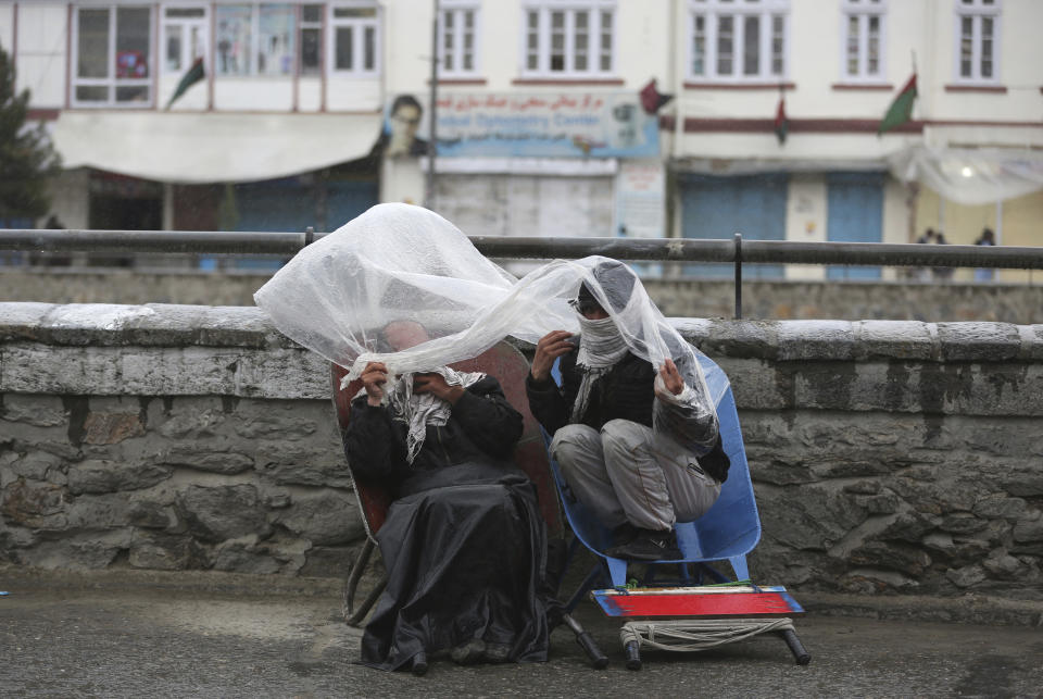 Laborers cover themself with a plastic sheet in the rain as they wait for customers in Kabul, Afghanistan, Monday, April 6, 2020. (AP Photo/Rahmat Gul)