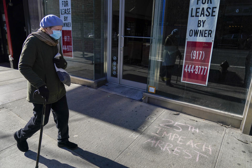 A pedestrian walks past a vacant commercial property and graffiti calling on President Trump to be removed from office and arrested, Sunday, Jan. 10, 2021, in the Hell's Kitchen neighborhood of New York. The boarded-up windows and For Rent signs are all over the place in Manhattan’s Hell’s Kitchen neighborhood. Nearby, the Broadway theaters are all dark. But the economic darkness brought on by the coronavirus pandemic has had a few bright spots. A couple of well-loved venues have gotten financial boosts, thanks to online fundraising campaigns and even a telethon. (AP Photo/Mary Altaffer)