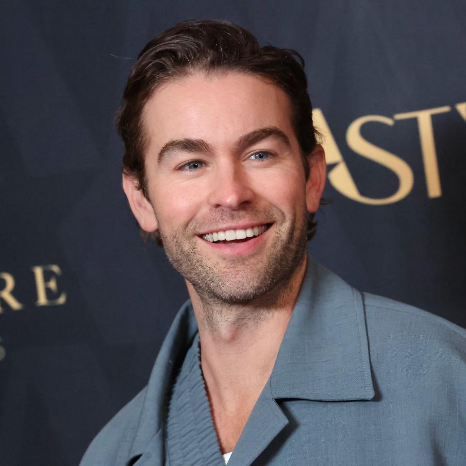 Chace Crawford smiles while wearing a casual jacket at a media event with a dark patterned backdrop