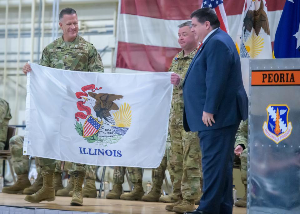 Major General Richard R. Neely, Commander of the Illinois National Guard, left, and Lt. Col. Jason Celletti, commander of the 1st Assault Helicopter Battalion, 106th Aviation Regiment, middle, present an Illinois flag to Gov. JB Pritzker during a mobilization ceremony for the regiment Tuesday, Feb. 7, 2023 at the 182nd Airlift Wing in Peoria.